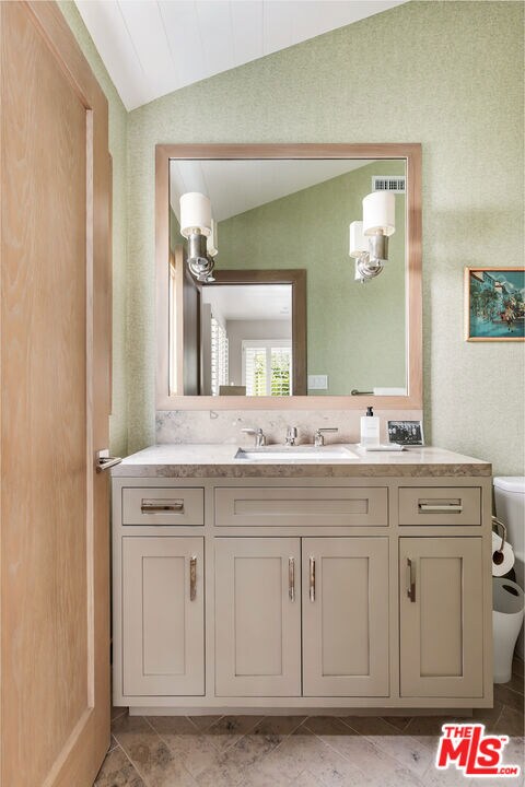 bathroom featuring toilet, vanity, and vaulted ceiling