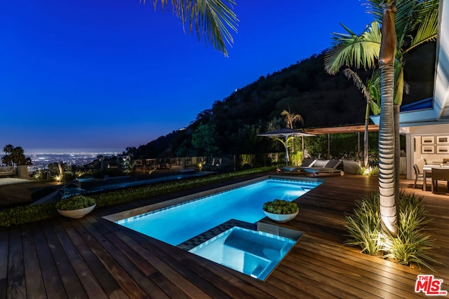 pool at dusk featuring a deck and an in ground hot tub