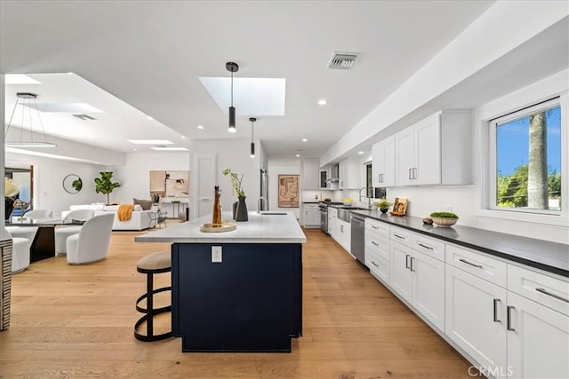 kitchen featuring white cabinets, a kitchen island, a kitchen breakfast bar, hanging light fixtures, and stainless steel dishwasher