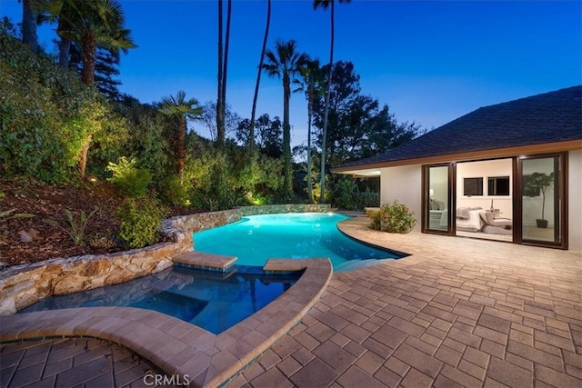 pool at dusk featuring a patio area and an in ground hot tub