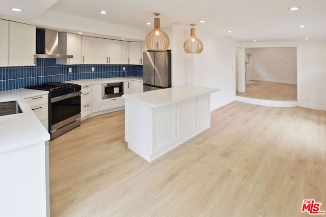 kitchen with light hardwood / wood-style floors, stainless steel appliances, decorative light fixtures, wall chimney range hood, and white cabinets