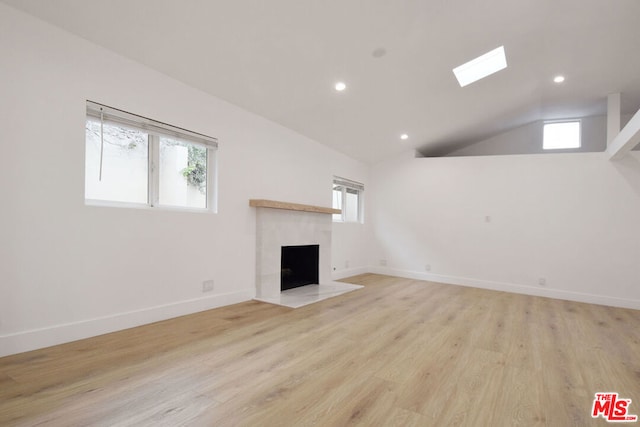 unfurnished living room with light wood-type flooring, a fireplace, a wealth of natural light, and vaulted ceiling