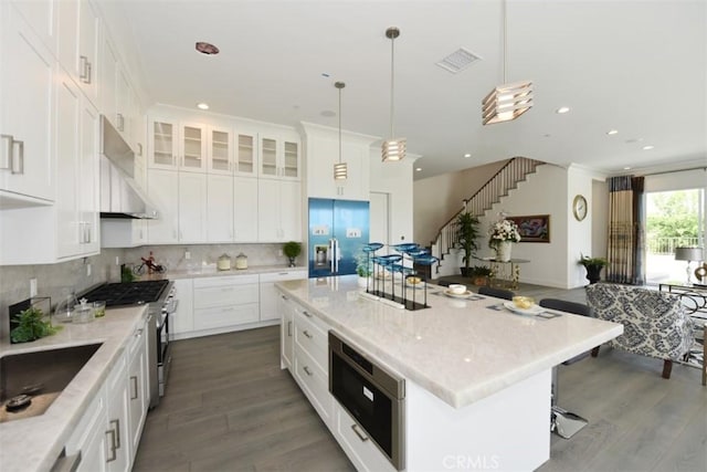 kitchen with exhaust hood, pendant lighting, a center island, built in appliances, and white cabinets