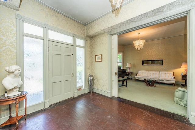 foyer entrance featuring dark wood-type flooring, a wealth of natural light, crown molding, and a notable chandelier