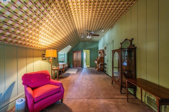 sitting room featuring ceiling fan, concrete flooring, lofted ceiling, and wood walls