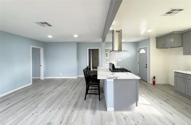 kitchen featuring light stone countertops, a kitchen bar, light hardwood / wood-style floors, gray cabinets, and island range hood