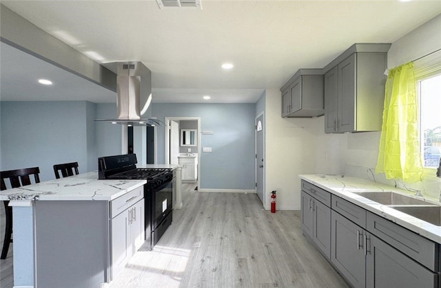 kitchen with range hood, a kitchen bar, black range oven, light wood-type flooring, and gray cabinetry