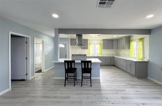 kitchen featuring range, a center island, wall chimney range hood, gray cabinetry, and a breakfast bar area