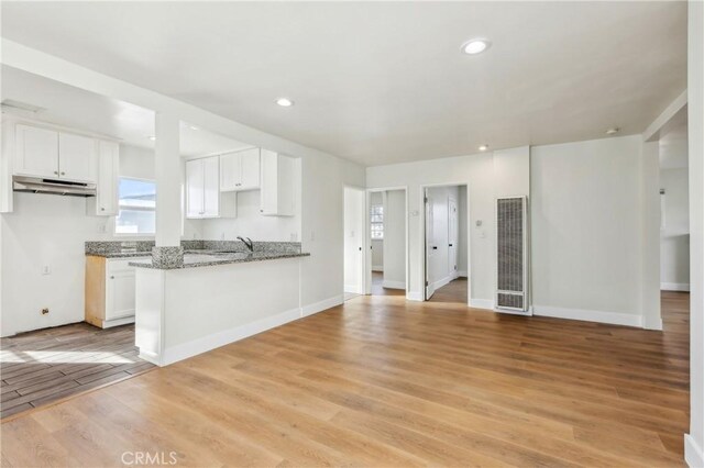 kitchen featuring kitchen peninsula, a healthy amount of sunlight, light hardwood / wood-style floors, white cabinetry, and stone counters