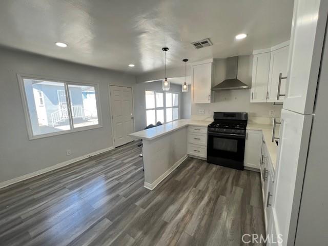 kitchen with kitchen peninsula, decorative light fixtures, wall chimney range hood, white cabinets, and black range with gas cooktop