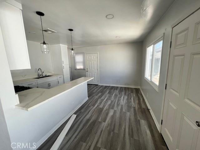 kitchen featuring kitchen peninsula, dark wood-type flooring, decorative light fixtures, white cabinetry, and sink