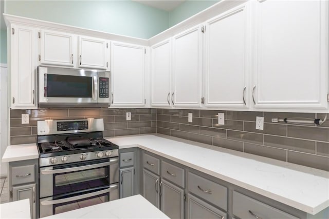 kitchen with stainless steel appliances, gray cabinetry, backsplash, and white cabinetry