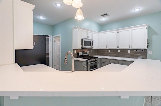 kitchen featuring white cabinetry, kitchen peninsula, gray cabinets, appliances with stainless steel finishes, and tasteful backsplash