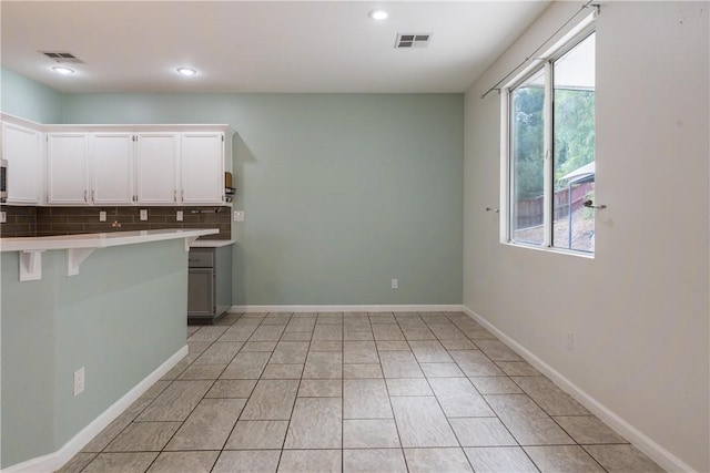 kitchen featuring tasteful backsplash, kitchen peninsula, light tile patterned floors, a breakfast bar area, and white cabinets