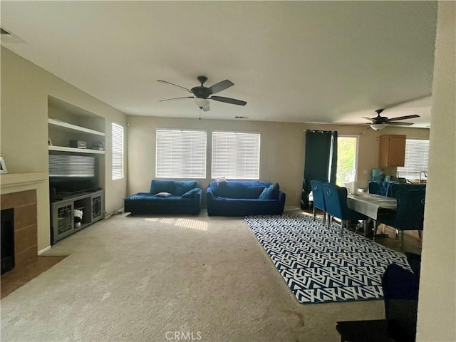 carpeted living room with ceiling fan, built in shelves, and a fireplace