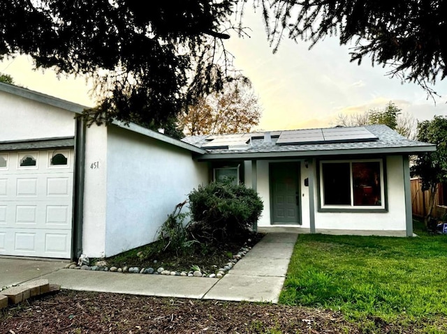 single story home featuring solar panels, a yard, and a garage