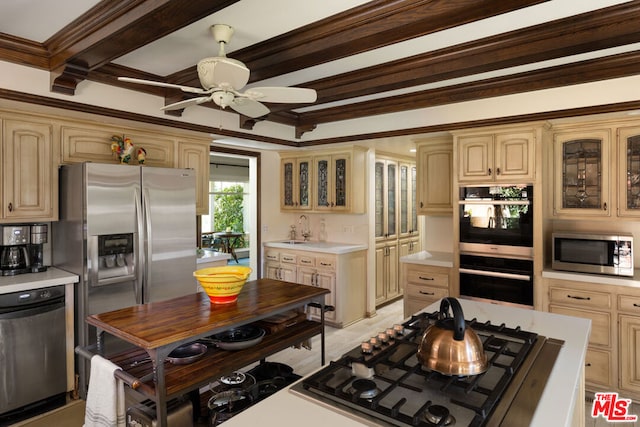 kitchen with sink, ceiling fan, appliances with stainless steel finishes, ornamental molding, and beamed ceiling