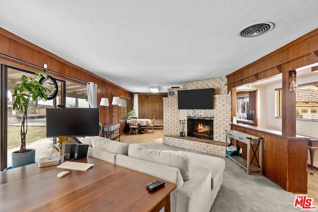 carpeted living room with a brick fireplace, wooden walls, and a textured ceiling