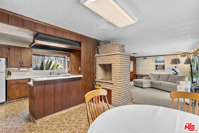 kitchen featuring a fireplace, kitchen peninsula, white fridge, and wooden walls