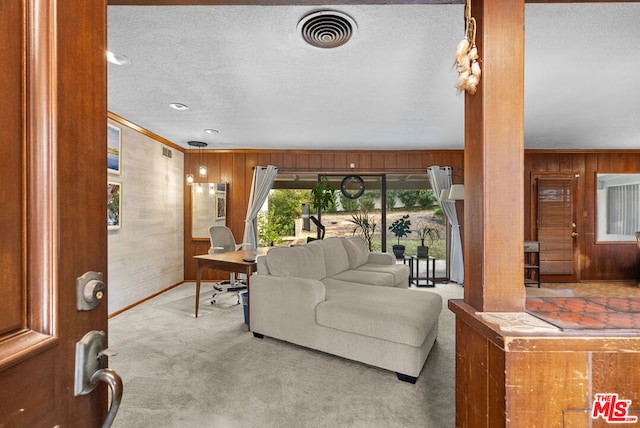 living room with light colored carpet, wooden walls, ornamental molding, and a textured ceiling