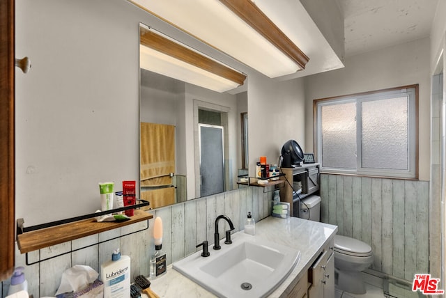 bathroom featuring baseboard heating, vanity, decorative backsplash, toilet, and wood walls