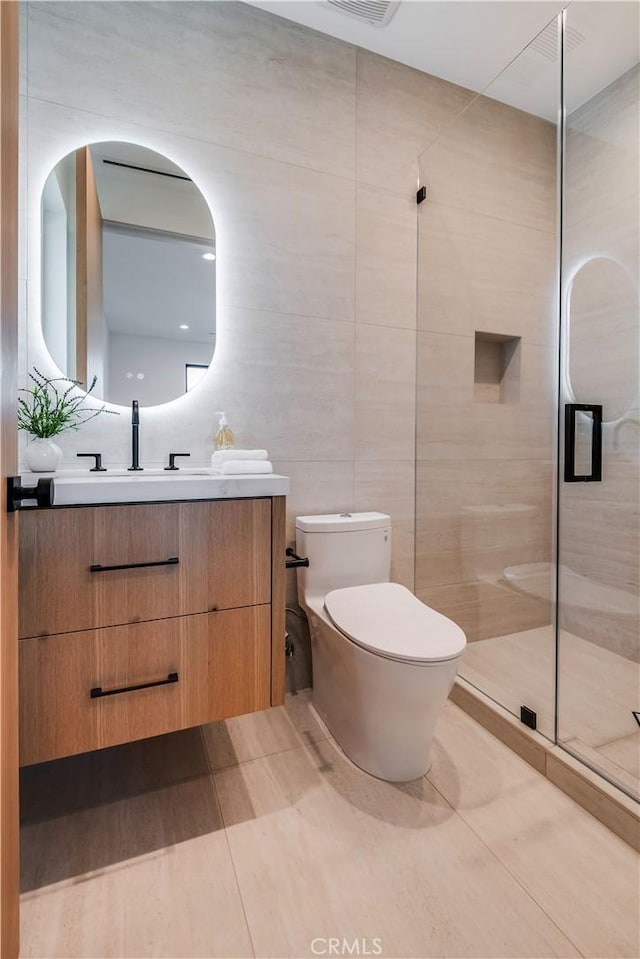 bathroom with toilet, a shower with shower door, tile patterned flooring, tile walls, and vanity