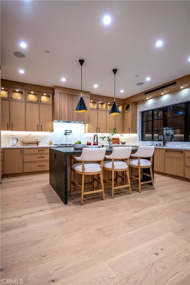 kitchen with a center island with sink, light hardwood / wood-style flooring, a kitchen breakfast bar, and pendant lighting