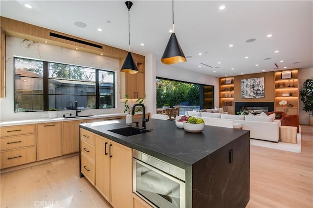 kitchen with pendant lighting, light brown cabinetry, sink, light hardwood / wood-style floors, and a kitchen island with sink