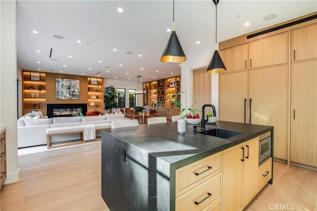 kitchen with light hardwood / wood-style flooring, light brown cabinetry, sink, stainless steel microwave, and a center island with sink