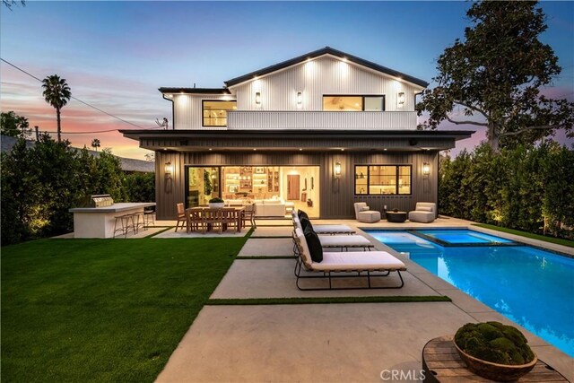 back house at dusk with a balcony, a patio area, a bar, and an outdoor living space