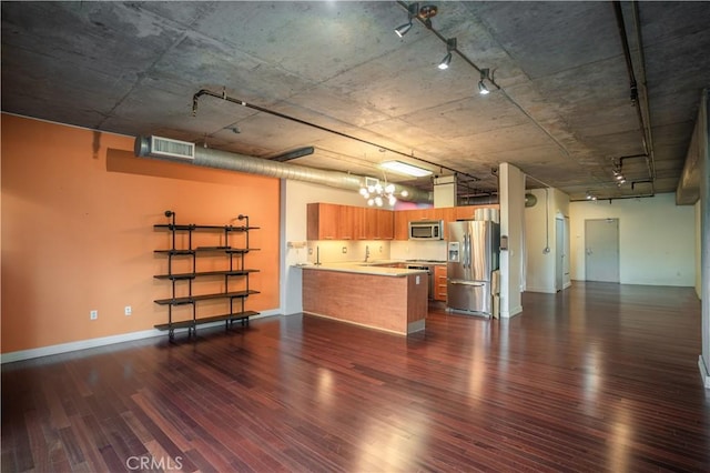 kitchen with appliances with stainless steel finishes, a chandelier, hanging light fixtures, kitchen peninsula, and dark wood-type flooring