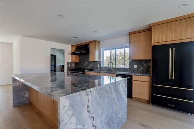 kitchen with a sink, black appliances, a large island, and wall chimney range hood