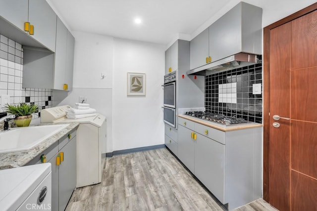 kitchen featuring washer and clothes dryer, tasteful backsplash, sink, oven, and light wood-type flooring