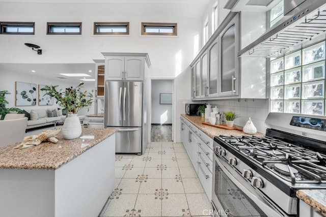 kitchen with stainless steel appliances, decorative backsplash, light tile patterned flooring, light stone countertops, and wall chimney exhaust hood