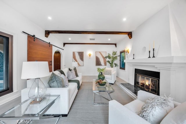 living room with beam ceiling, a barn door, a fireplace, and hardwood / wood-style floors