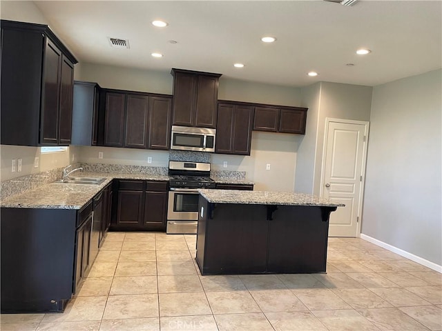 kitchen featuring light tile patterned floors, stainless steel appliances, light stone counters, and a center island