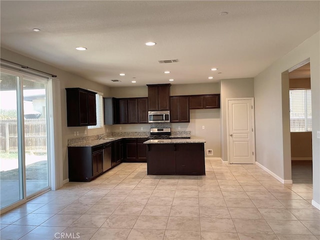 kitchen featuring appliances with stainless steel finishes, sink, light stone counters, and a kitchen island