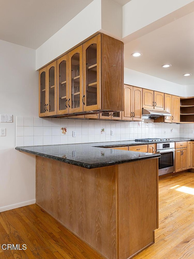 kitchen with kitchen peninsula, dark stone counters, stainless steel appliances, and light hardwood / wood-style floors