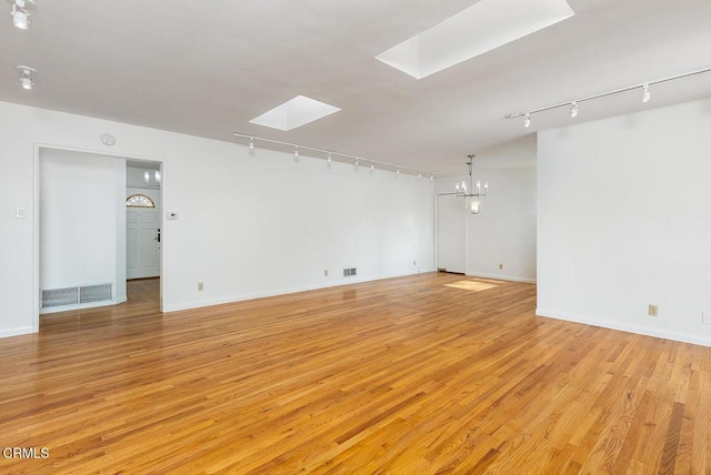 empty room with a skylight, a notable chandelier, and light hardwood / wood-style flooring