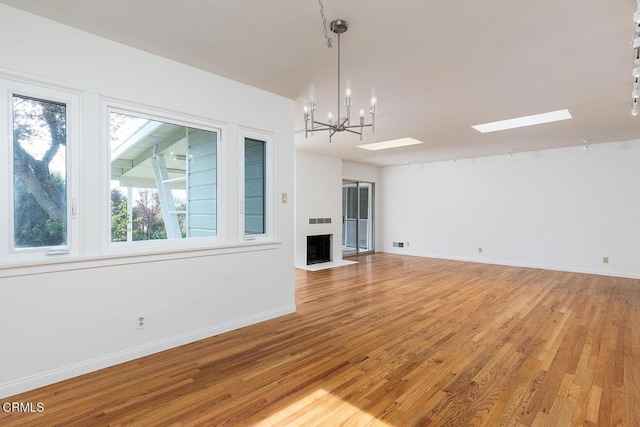 unfurnished living room with a skylight, hardwood / wood-style floors, and a notable chandelier