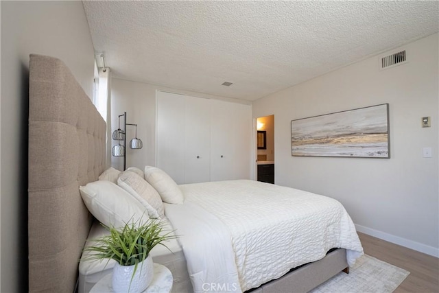 bedroom with a textured ceiling, ensuite bathroom, a closet, and hardwood / wood-style floors