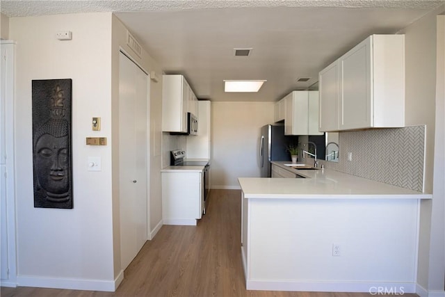 kitchen with appliances with stainless steel finishes, white cabinetry, decorative backsplash, kitchen peninsula, and light hardwood / wood-style flooring