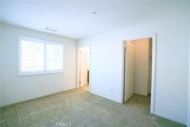 unfurnished bedroom featuring a spacious closet, a closet, and light carpet