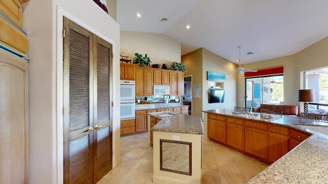 kitchen with pendant lighting, a center island, white appliances, light stone countertops, and light tile patterned floors