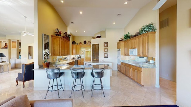 kitchen featuring kitchen peninsula, white appliances, light tile patterned flooring, high vaulted ceiling, and a breakfast bar