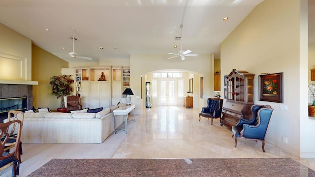 living room with ceiling fan, a towering ceiling, and a tiled fireplace