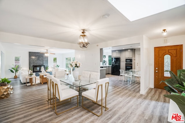 dining space with ceiling fan with notable chandelier, a large fireplace, and light hardwood / wood-style flooring