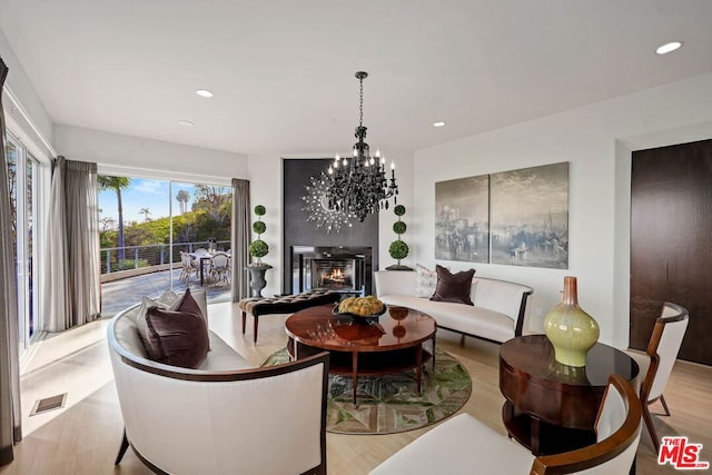 living room featuring a large fireplace, a chandelier, and light hardwood / wood-style flooring