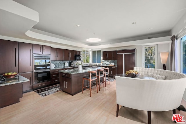 kitchen with tasteful backsplash, a kitchen island, black appliances, a tray ceiling, and dark brown cabinets