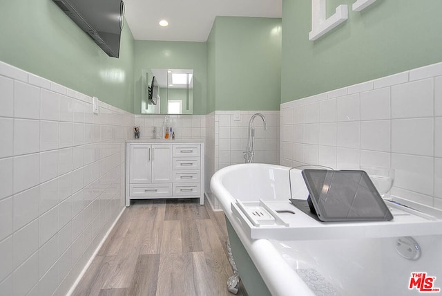 bathroom featuring vanity, tile walls, hardwood / wood-style floors, and a tub